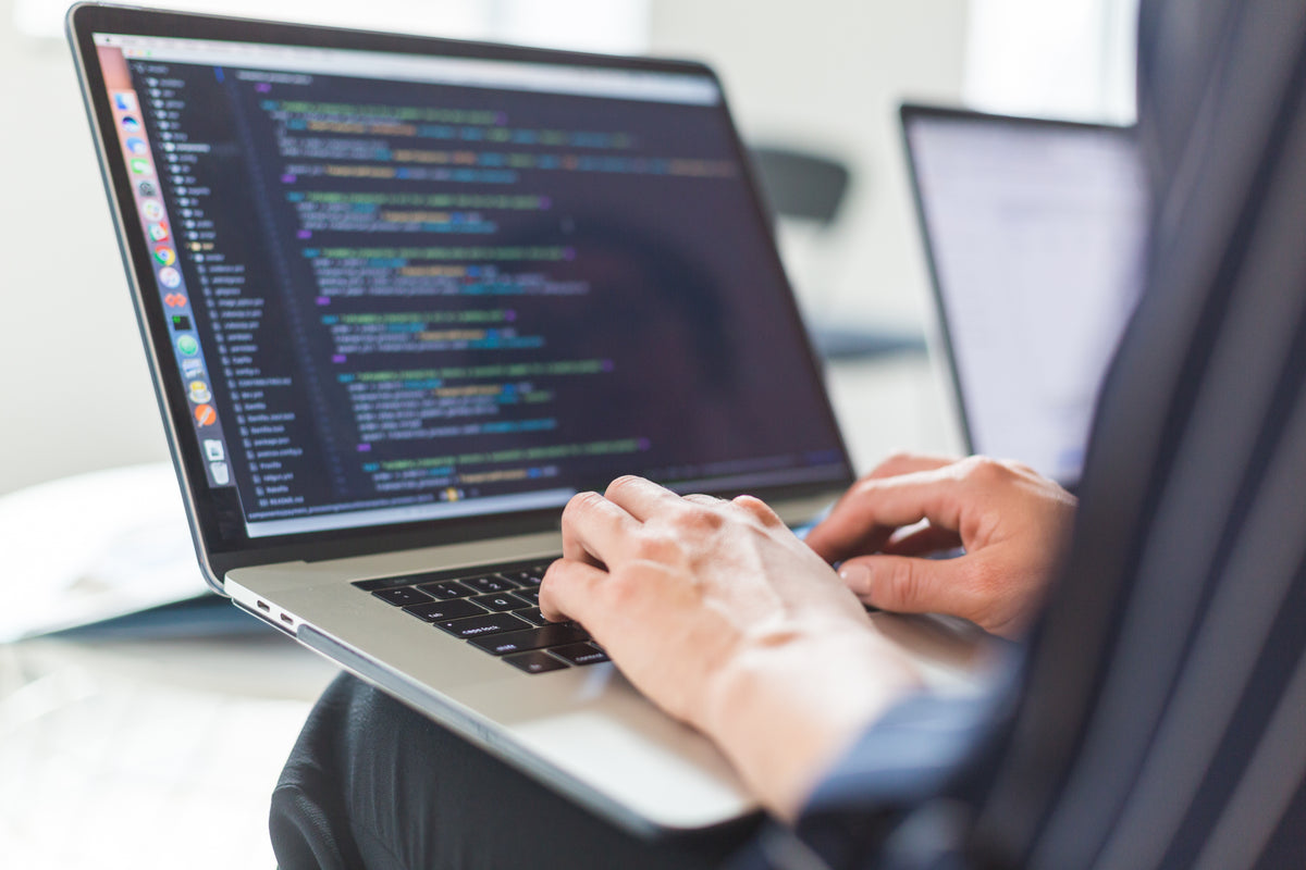 Hände tippen auf einem Laptop mit geöffnetem Code-Editor